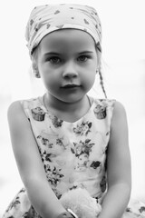 Young girl with braided hair wearing a patterned dress and headscarf is playing with toys on a grassy field, surrounded by colorful play items and a joyful atmosphere