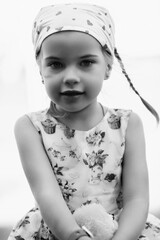 Young girl with braided hair wearing a patterned dress and headscarf is playing with toys on a grassy field, surrounded by colorful play items and a joyful atmosphere