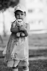 Young girl with braided hair wearing a patterned dress and headscarf is playing with toys on a grassy field, surrounded by colorful play items and a joyful atmosphere