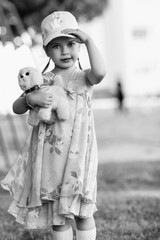 Young girl with braided hair wearing a patterned dress and headscarf is playing with toys on a grassy field, surrounded by colorful play items and a joyful atmosphere