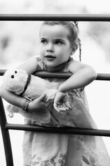Young girl with braided hair wearing a patterned dress and headscarf is playing with toys on a grassy field, surrounded by colorful play items and a joyful atmosphere