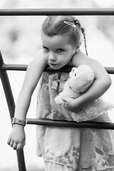 Young girl with braided hair wearing a patterned dress and headscarf is playing with toys on a grassy field, surrounded by colorful play items and a joyful atmosphere