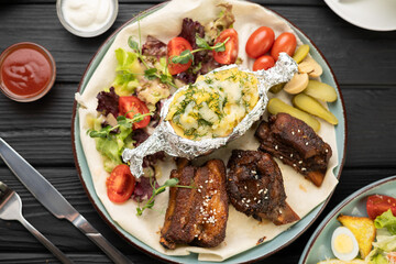 Juicy grilled pork ribs with baked potatoes vegetables and tomato ketchup on plate in restaurant