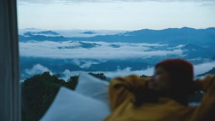 Blurred of a woman lying on the bed and looking at a beautiful nature view outside the window on foggy morning