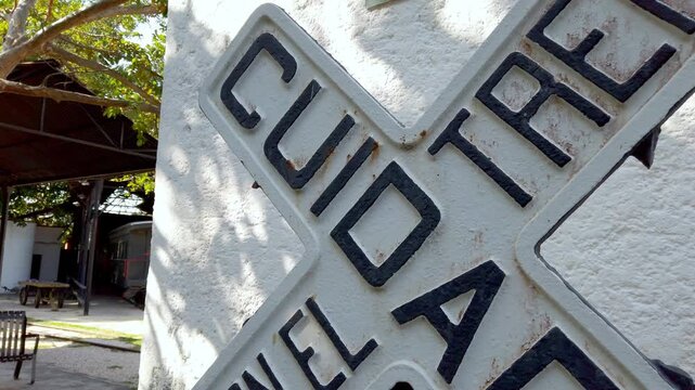 Pan left shot of a railroad crossing sign mounted on a textured white wall outdoors.