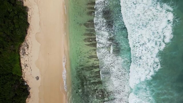 Aerial drone shot of Pantai Pasir Putih coastline in Karangasem Bali Indonesia showing white sand beach, turquoise water, reef patterns and waves breaking along shore.