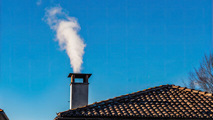 White smoke rises from the chimney concept. Chimney emitting steam against a bright blue sky.