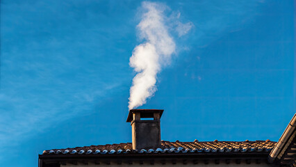 White smoke rises from the chimney concept. A chimney emitting smoke against a clear blue sky backdrop.