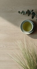 Warm light illuminates a cup of green tea beside eucalyptus and grass.