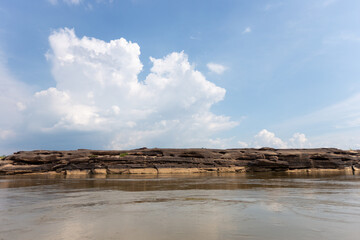 A panoramic summer landscape of the sea and sky featuring white clouds reflecting over the ocean water with distant mountains and a sandy beach for nature travel and tourism
