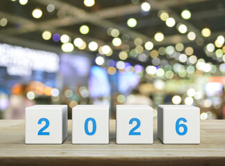 2026 letter on white block cubes on wooden table over blur light and shadow of shopping mall, Happy new year 2026 cover concept