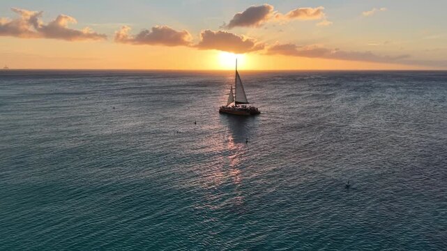 Drone zoom in in on sailboat crossing the setting sun off the island of Aruba