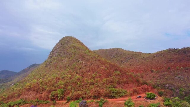 A drone performs a wide orbit around a conical Cerrado hill while a 4x4 truck sits on the red dirt road at its base on the route to Tocantins.