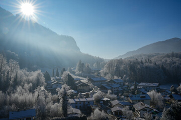 Picturesque, wintry Aschau im Chiemgau, Bavaria. Trees and roofs are covered with a thick layer of frost, surrounded by snow-capped mountains in the bright winter sun.