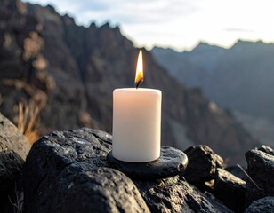 Candle burning atop rocks, scenic mountains at sunrise