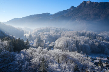 Aerial view of a winter landscape with hoarfrost in the Priental valley in the Chiemgau Alps. Several snow-covered houses can be seen in the valley amid the frosty forests.