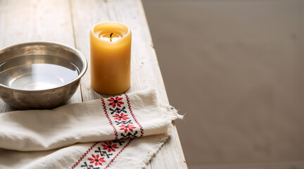 Ritual setting with a bowl of water and a lit candle on a wooden table. Traditional embroidered cloth and folk elements. Spiritual ceremony concept with copy space