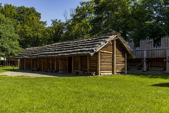 Ancient wooden longhouse reconstruction in archaeological open-air museum, historical timber hut in sunny garden