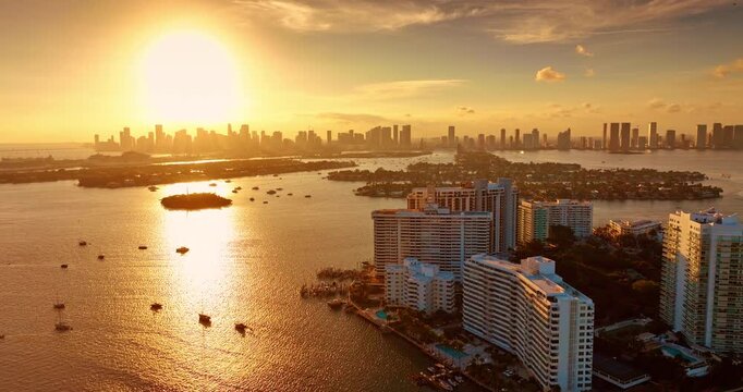 Golden sunset lighting Biscayne Bay with multiple vessels on. View on silhouettes of high-rises in Miami skyline at backdrop. Aerial view.