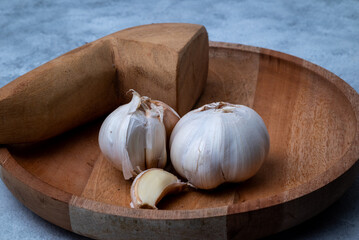 Fresh garlic is placed in a mortar and pestle on a marble-patterned wooden table.