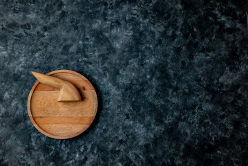 Top view of a round wooden plate with wooden tools on a dark textured background. Minimalist concept with ample copy space.