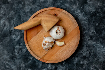 Fresh garlic is placed on a wooden mortar and pestle against a dark background.