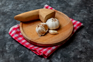 Fresh garlic is placed on a wooden mortar and pestle with a red and white checkered cloth as the base.