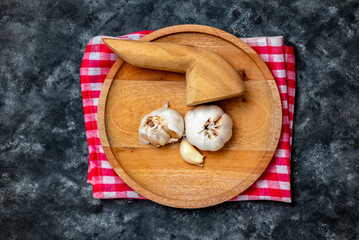 Fresh garlic is placed on a wooden mortar and pestle with a red and white checkered cloth as the base.