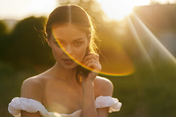 Young woman in a white off shoulder dress, radiating warmth and confidence, basking in golden...