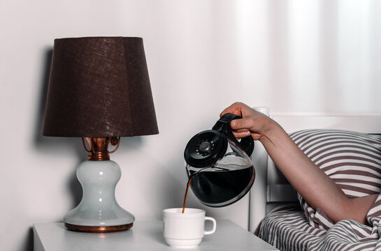 Hand pouring coffee into cup on bedside table in early morning