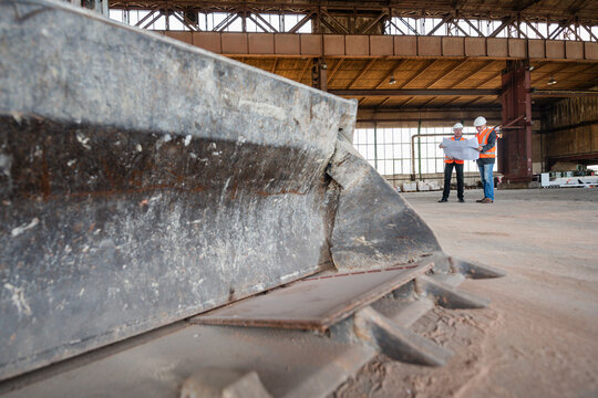 Employees meeting beside bulldozer in large industrial production hall
