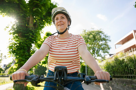 Person cycling outdoors wearing helmet and striped shirt in sunshine