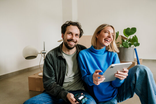 Happy couple planning future at home with moving boxes and tablet