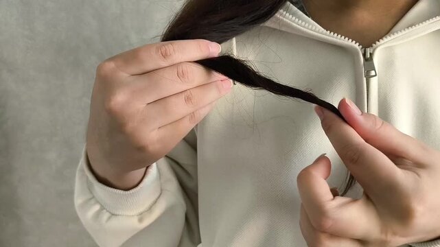 Young brunette woman winding thin ends of hair on her finger. The girl touches the dry ends of her hair. The concept of hair loss.