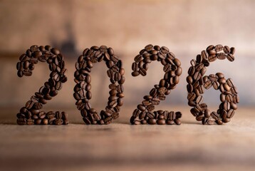 The numerals "2026" creatively formed by arranging roasted coffee beans on a wooden table, set against a softly blurred cozy caf&eacute; interior background with warm lighting. A few lighter beans add subtle