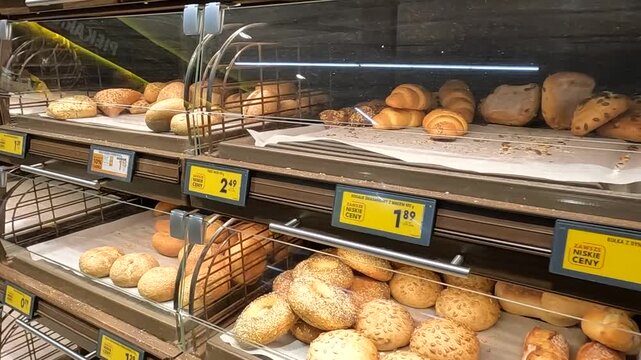 KRAKOW, POLAND - DECEMBER 23, 2025: Small rolls, both sweet and savory, line the self-service aisle in the store. Prices are displayed on large labels.