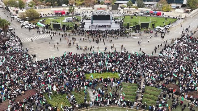 An aerial view of thousands of Syrians celebrating the end of the war in Damascus, carrying Syrian flags.