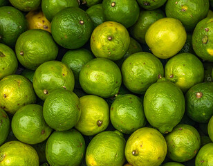 Close-up of numerous round green and yellow citrus fruits, piled together