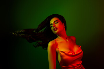 Fototapeta premium Stunning young woman posing in gradient lighting, wearing chic satin dress, radiating glamour and charm