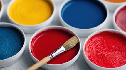 A vibrant array of paint pots in various colors, with a brush resting in the red paint, perfect for artistic projects and creative expression.