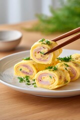 closeup of omelet rolls with ham and cheese, on a white plate, using chopsticks to pick up one omelet rollt, wooden table background, warm color tone