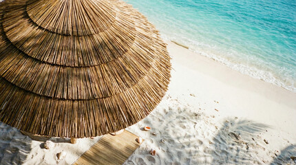 Top-down close-up of a straw beach umbrella and sun lounger on white sand.