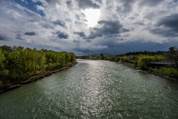 River flowing through green park under dramatic cloudy sky