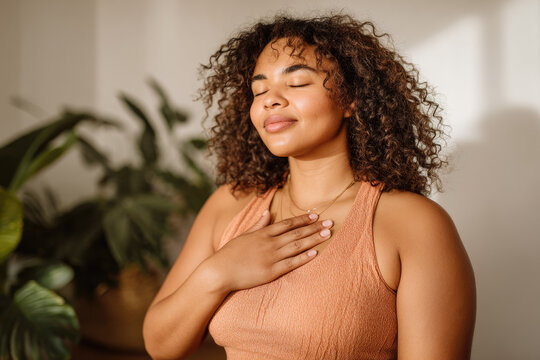 Plus size woman practicing yoga with peaceful smile showing self love and mindfulness in sunlit room with green plants in background for body positivity