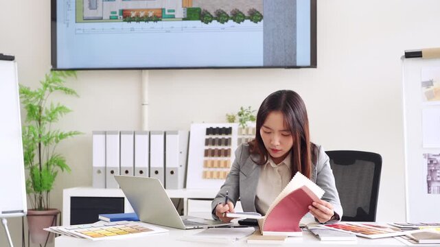 Young asian female interior designer or architect working on creative project with drawing, material sample , laptop computer in office. Business of Real estate, home decoration , renovation concept.