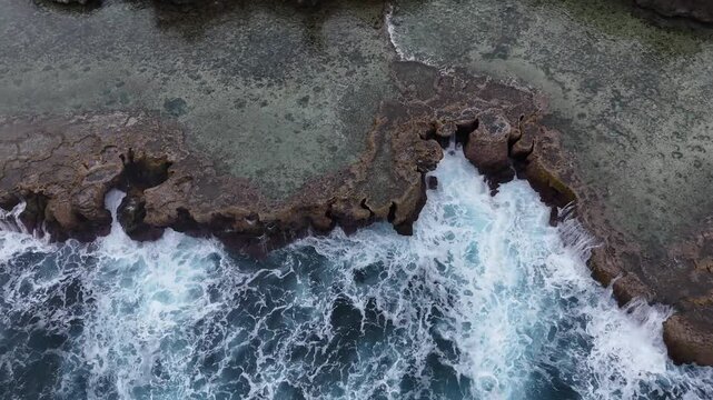 Stunning top-down aerial drone view of turquoise waves breaking over a vibrant coral reef in Tonga. A beautiful abstract pattern of white surf and deep blue Pacific water.