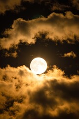 Full moon shines brightly through golden clouds in a dark nighttime sky. Use: travel poster, astronomy book cover.