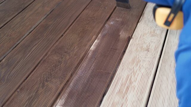 Brown oil for protection of wood by staining. Painting a larch for protecting and pests. Woodworker applying finish to terrace deck board. Repairman varnishing with brush wooden plank floor surface.