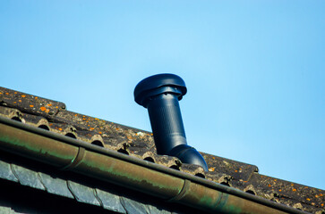 Black ventilation pipe on a weathered roof against a clear blue sky