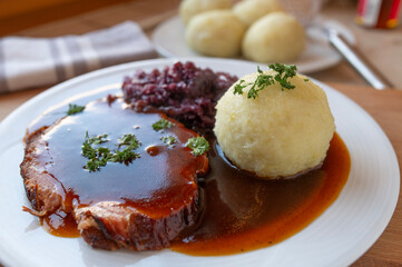 Delicious homemade roast pork with red cabbage, potato dumpling and gravy on a plate. Traditional german food